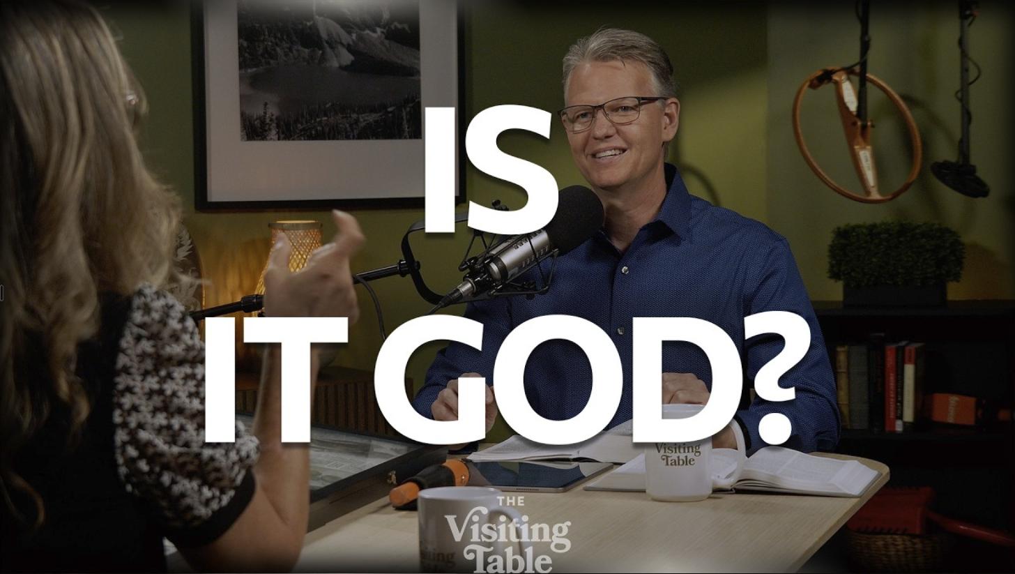 Julie Norton gestures while talking with Ken Norton across The Visiting Table, with bold text reading "Is It God?"