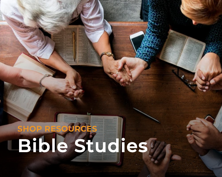 There's a diverse group of people holding hands and praying over their Bibles.