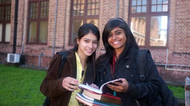 Two teenage girls smiling while holding school books.