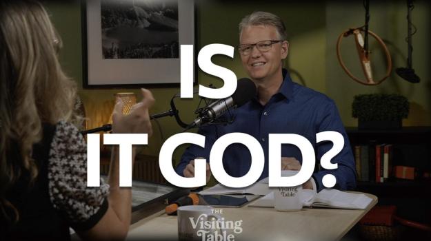 Julie Norton gestures while talking with Ken Norton across The Visiting Table, with bold text reading "Is It God?"