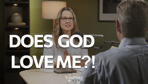 Julie Norton speaks with Ken Norton across a table on The Visiting Table set, with bold text reading "Does God Love Me?!"Ken and Julie Norton discuss what God thinks of us on The Visiting Table.